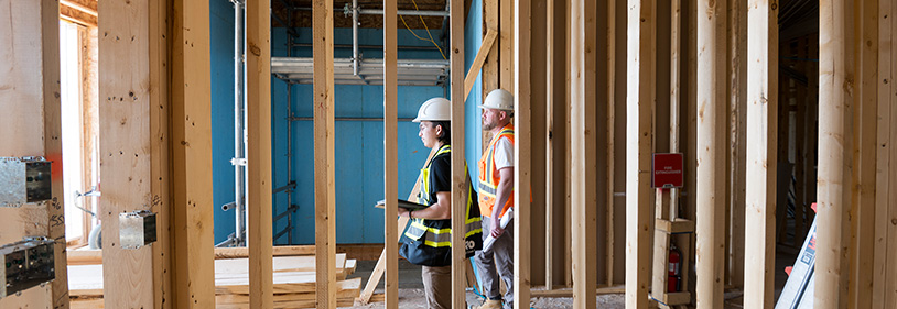 2 construction workers seen through framing of wall.