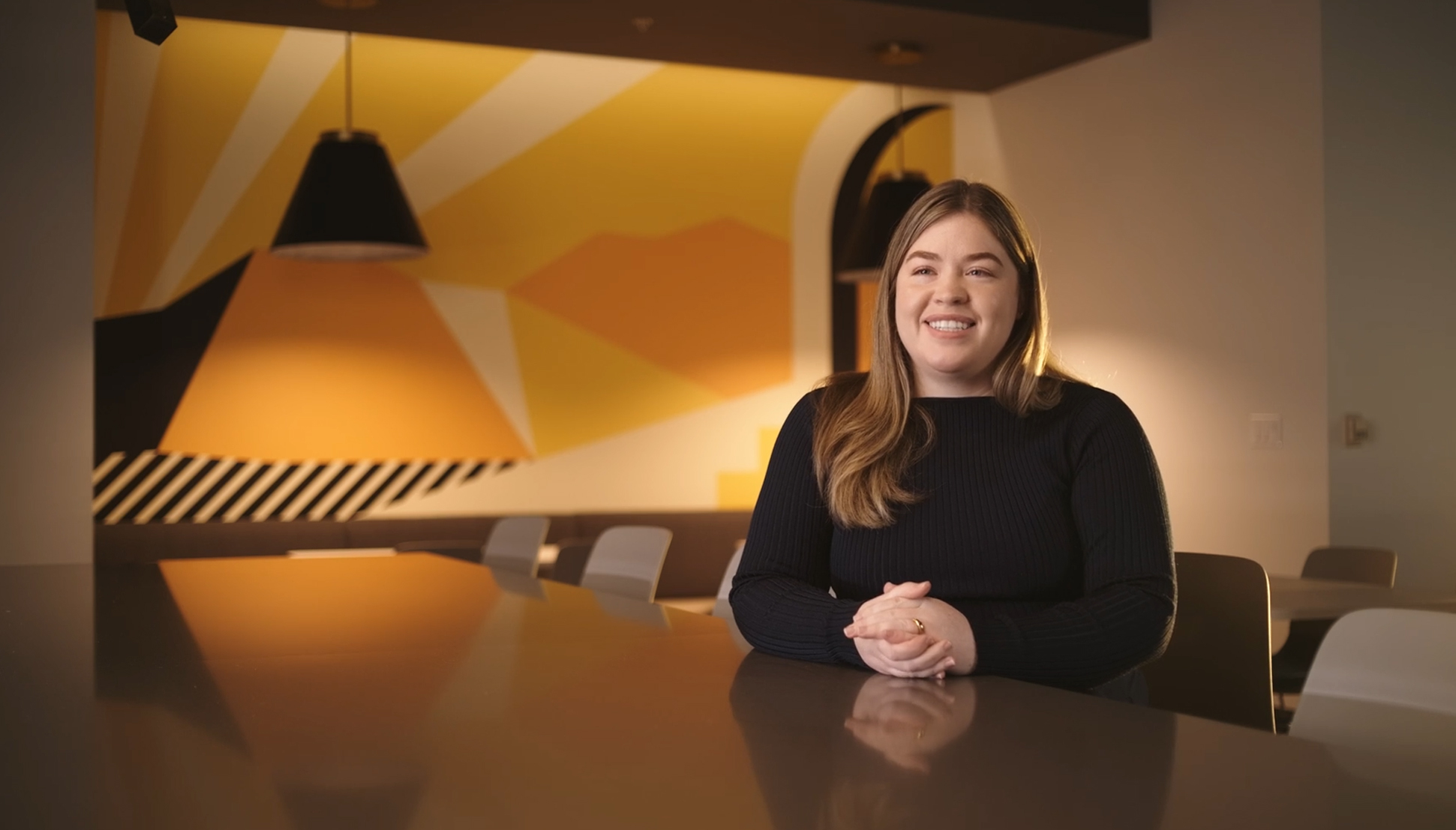 Photo of woman sitting at boardroom table with ambient lights and Yellow graphic behind her.