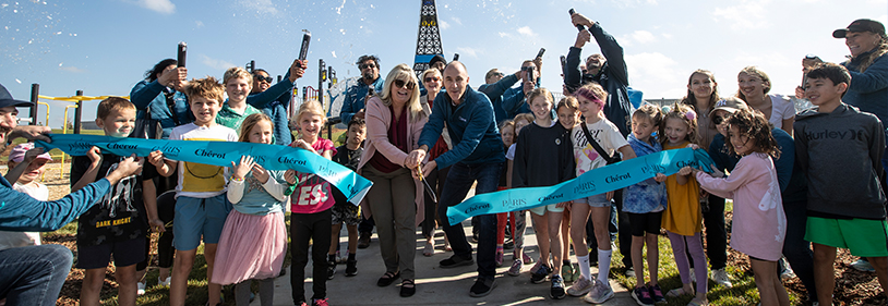 Ribbon cutting with lots of people holding the blue ribbon.